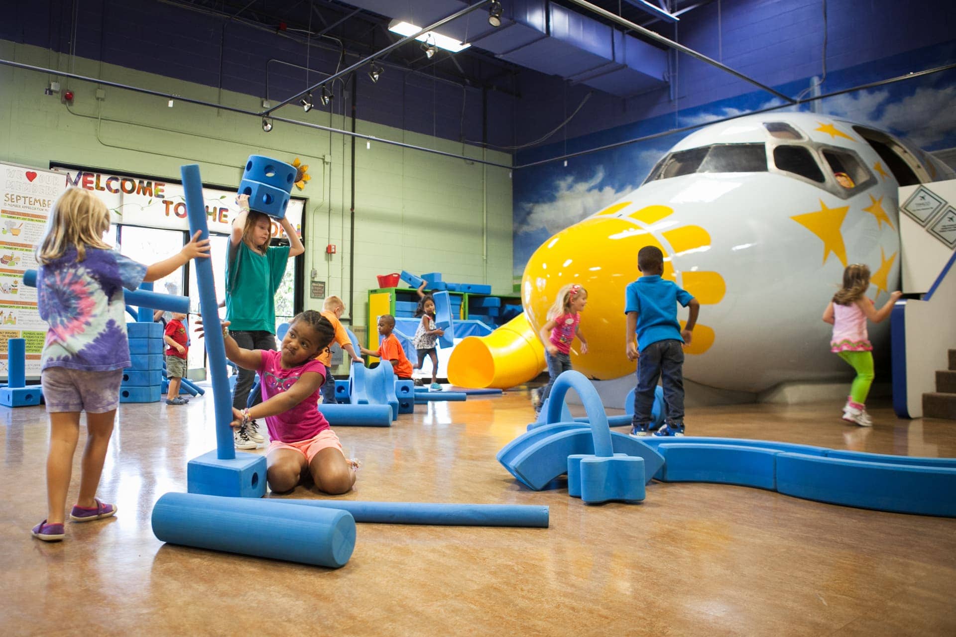 Indoor play area at Miriam P. Brenner Children's Museum with kids exploring airplane-themed exhibits.