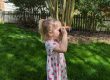 Child looking through binoculars in backyard.